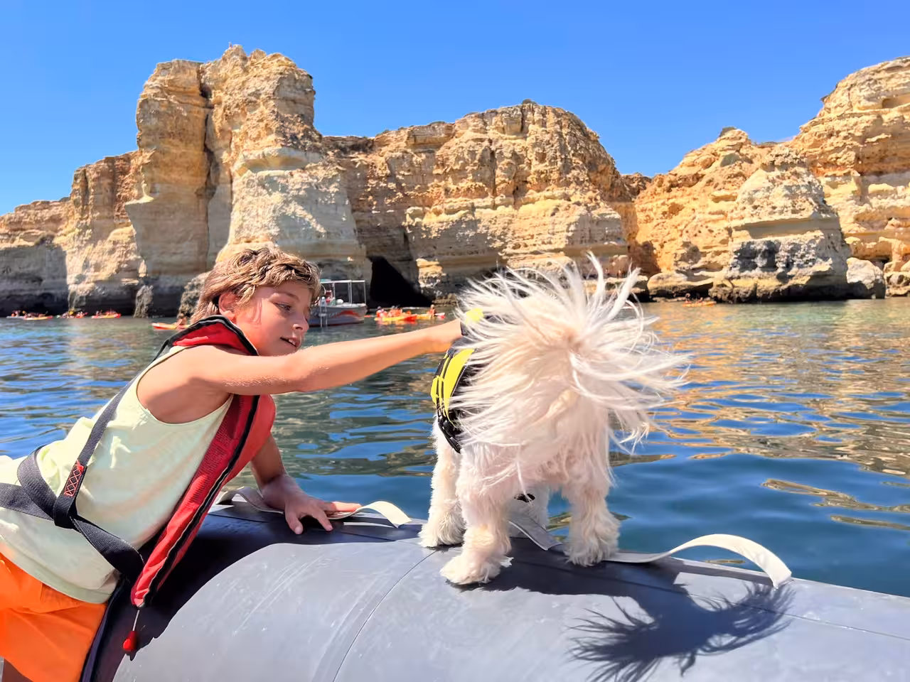 Smiling child and small dog in life jacket on boat near Benagil cliffs during family-friendly Algarve dolphin tour