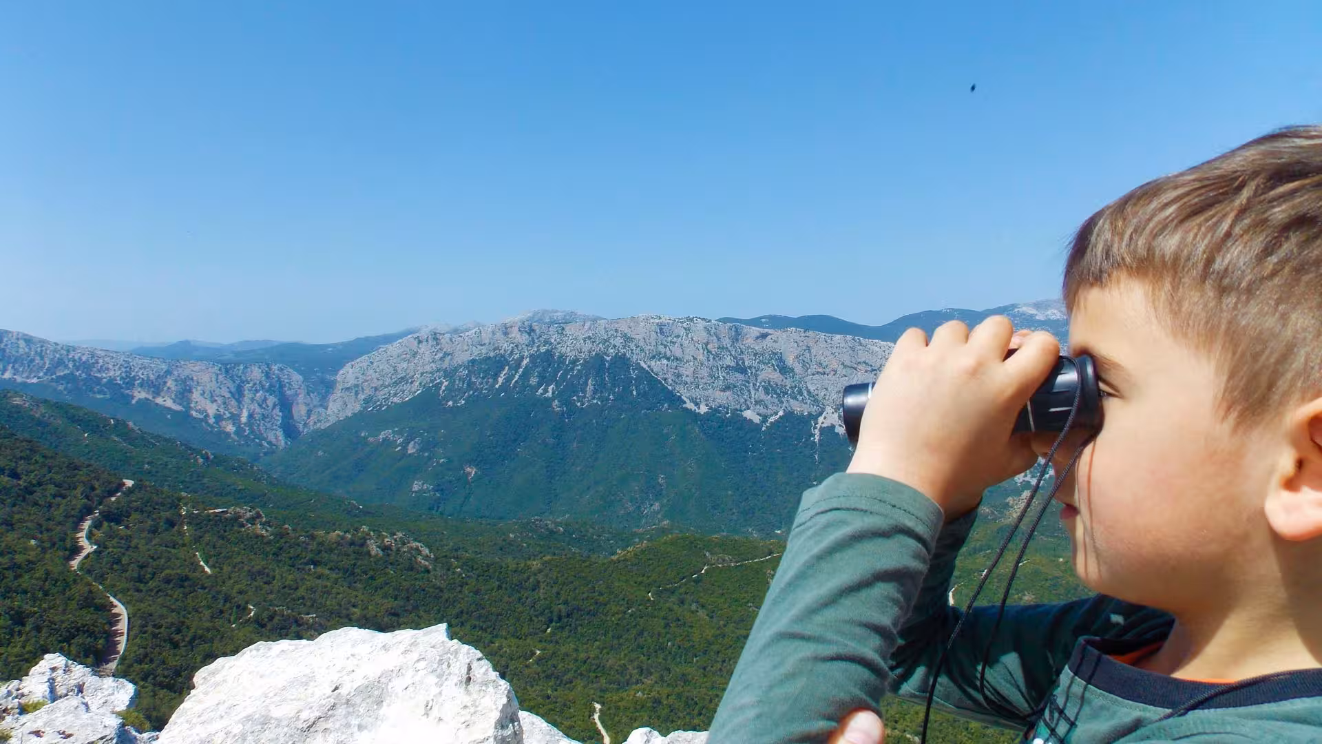 Child using binoculars to admire breathtaking mountain views during a donkey hike near Dorgali.