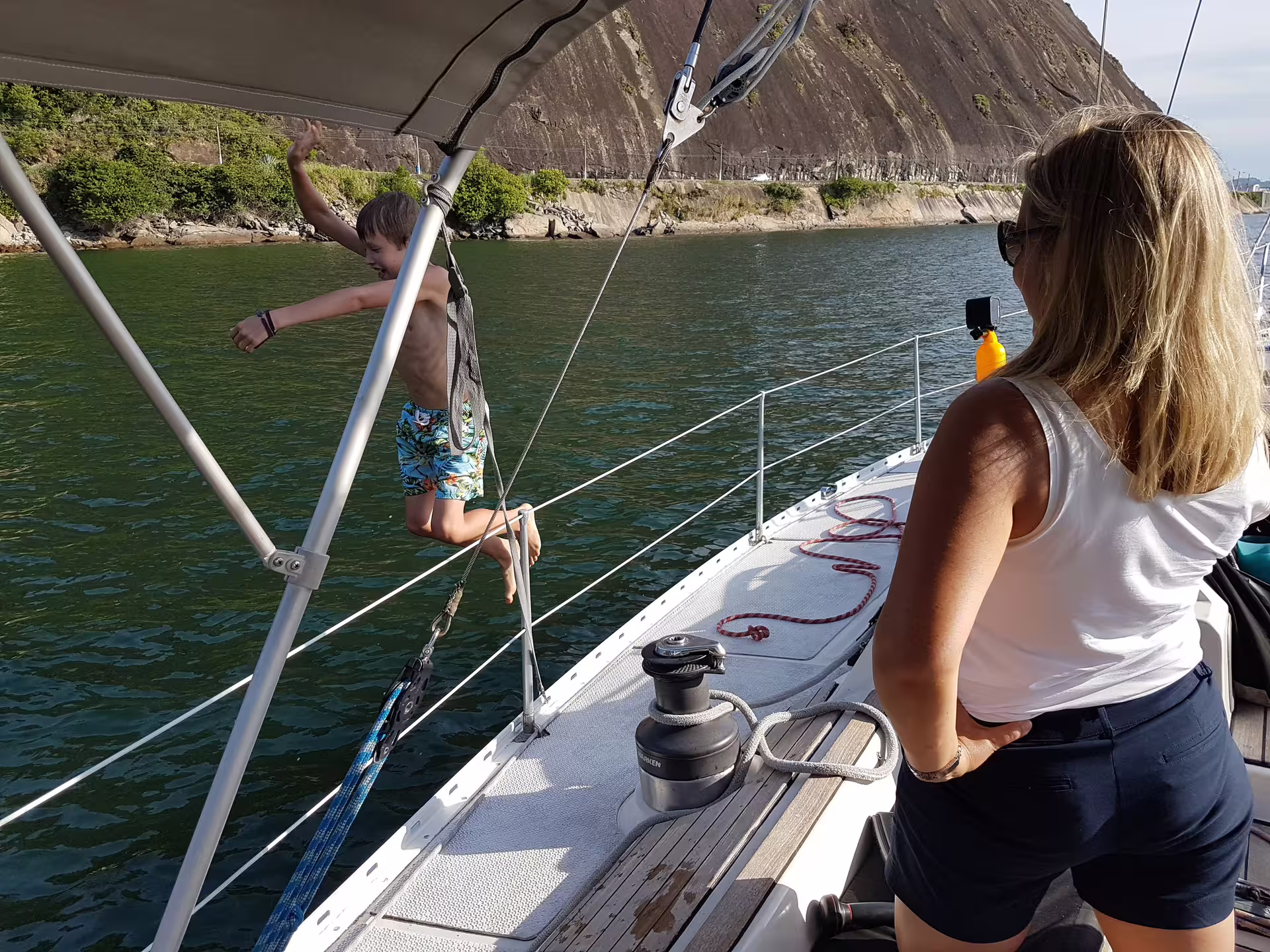 Child joyfully jumping off a sailboat deck into the ocean, supervised by an adult on a private sailing tour.
