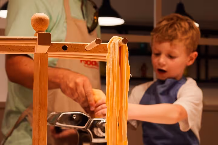 Child learning to make fresh pasta with assistance in a Barcelona cooking class, enhancing culinary skills and creativity.