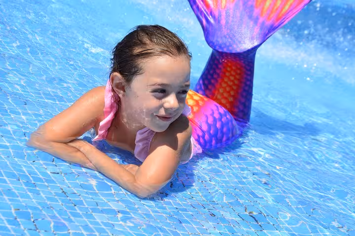 Smiling child in a vibrant mermaid tail during a private photoshoot in Hersonissos pool.