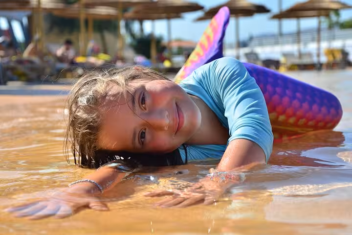 Joyful child wearing a mermaid tail, playfully lying in the water at a Hersonissos photoshoot setting.