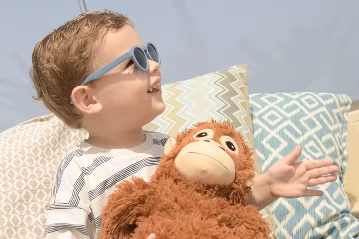 Joyful child in sunglasses enjoys Hersonissos sun with plush monkey, perfect for family photoshoot memories.