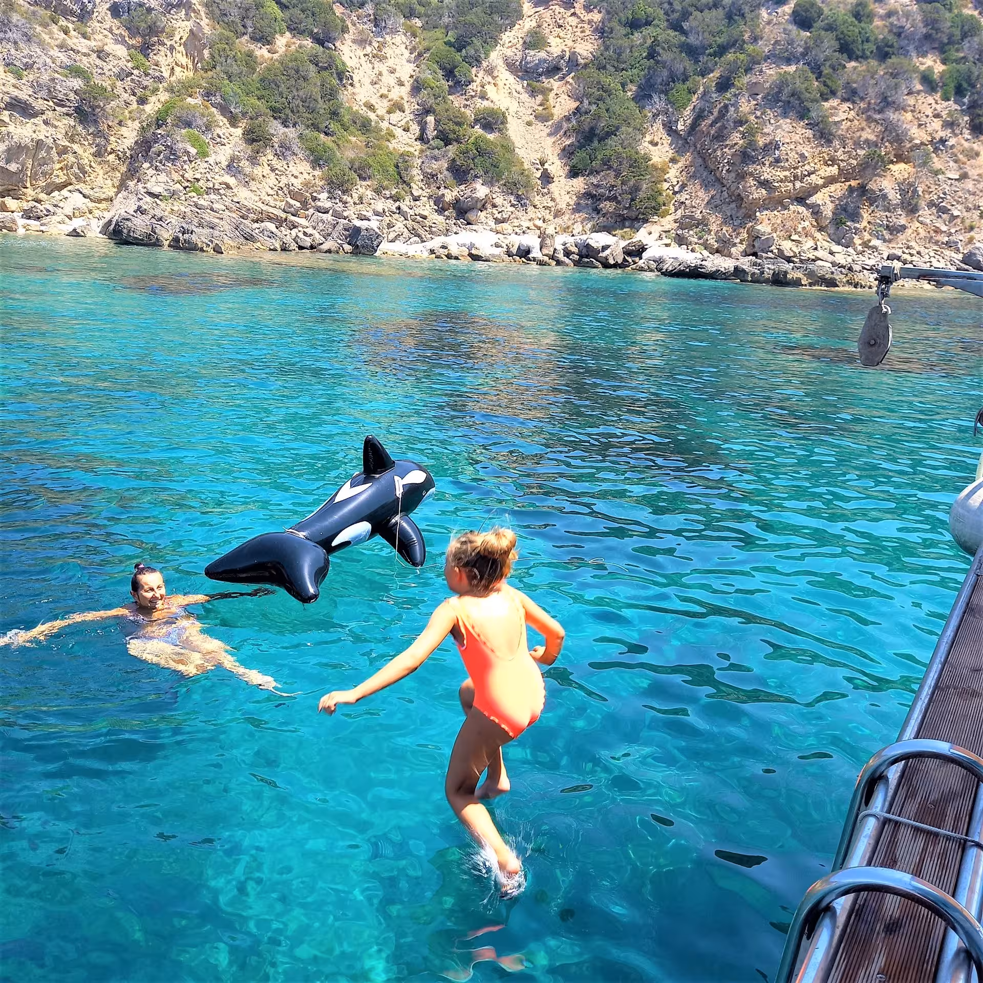 Child jumps into turquoise sea with inflatable toy on a Capo Caccia marine area fishing tour in Alghero.