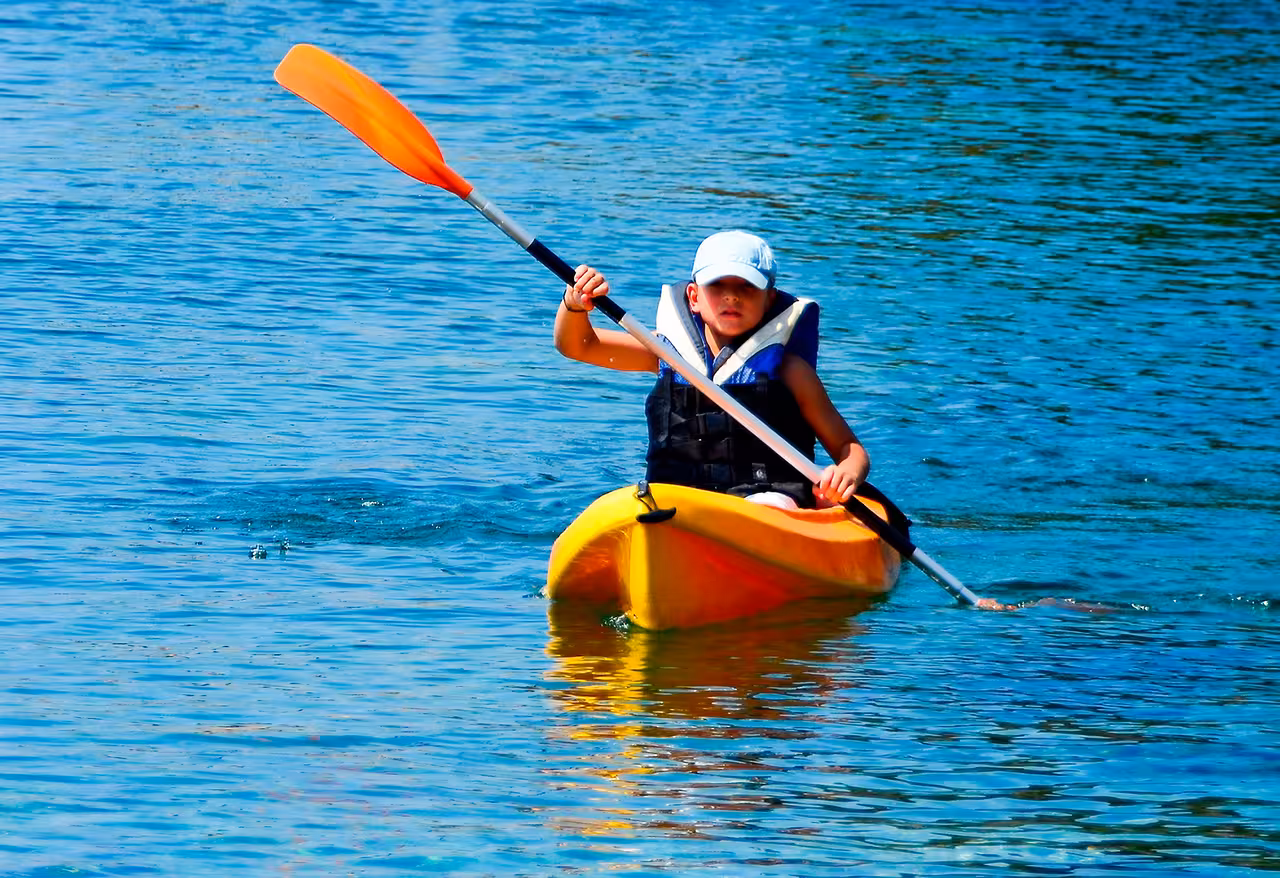 Child in life jacket paddling a yellow kayak on calm blue water, enjoying a family-friendly kayak rental adventure