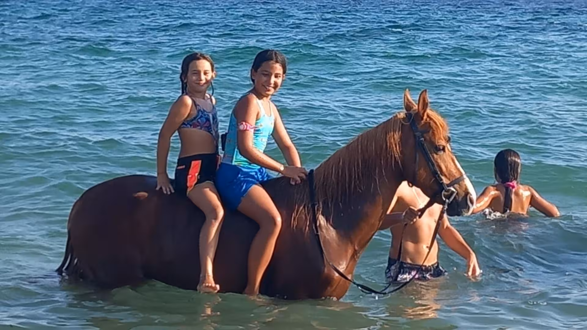 Two children riding a horse in the sea during a fun-filled Cagliari sunrise dive tour.
