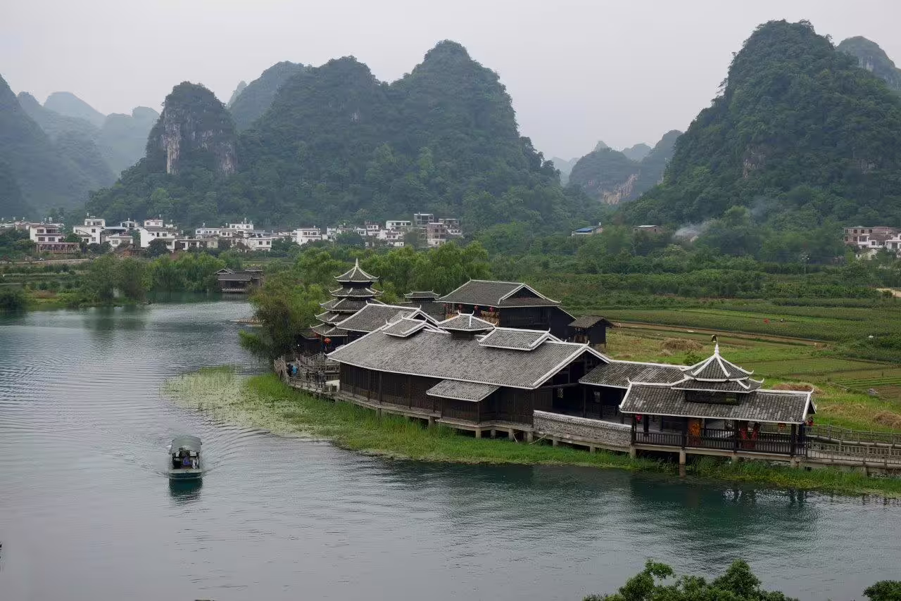 Scenic view of traditional Chinese architecture by the Li River with karst mountains in the background.