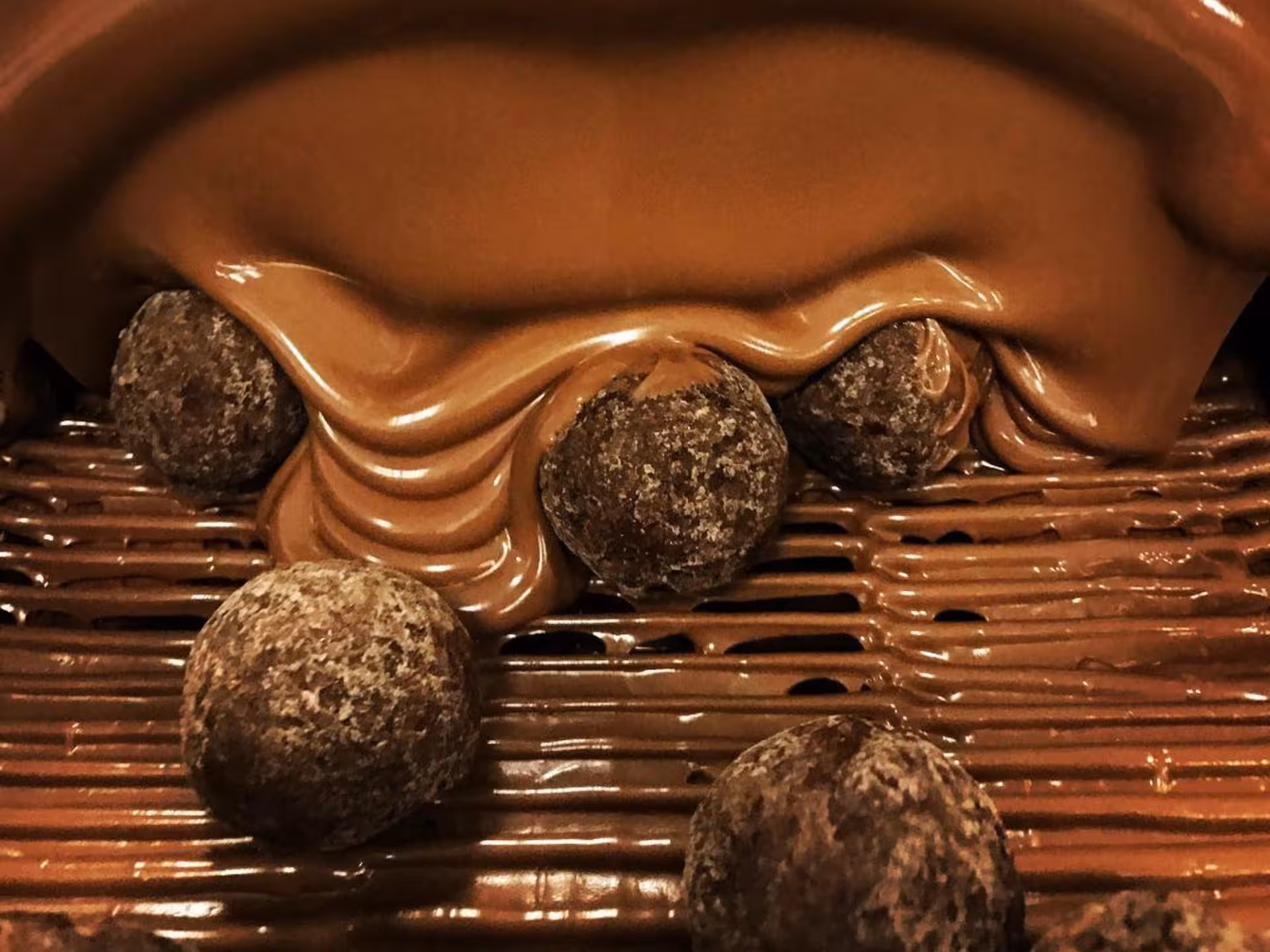 Rich melted chocolate cascading over truffles at Alessandria chocolate factory tour, showcasing delectable creations.