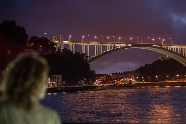 Night view of Arrábida Bridge over the Douro River with city lights, seen from a Christmas dinner cruise in Porto.