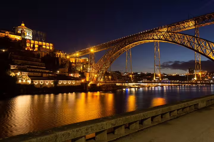 Illuminated Dom Luís I Bridge at night reflecting on the Douro River during a Christmas dinner cruise in Porto.