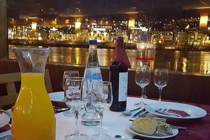 Elegant dinner table setup with wine and juice on a river cruise, offering a view of Porto's illuminated waterfront at night.