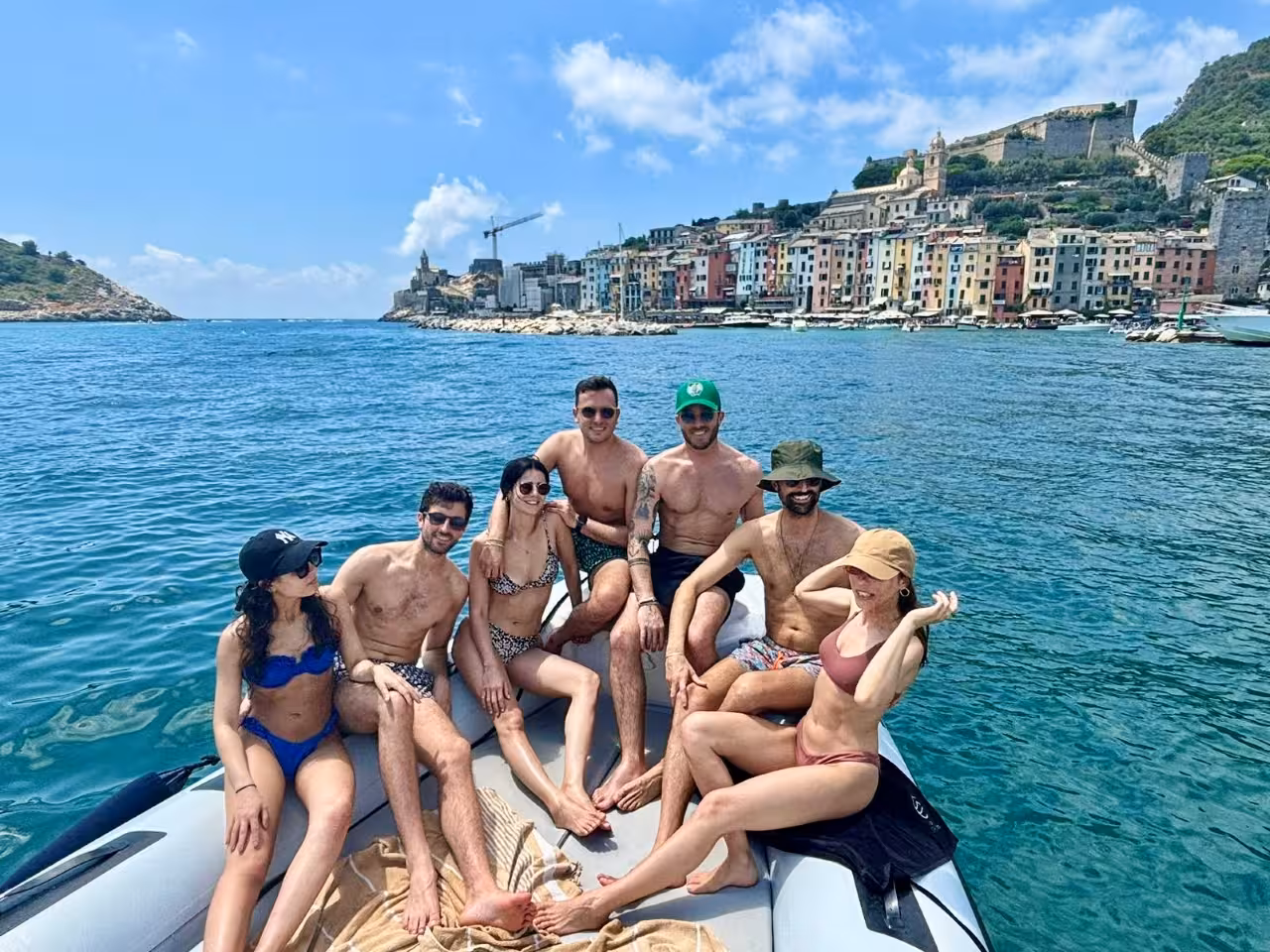 Group relaxing on a boat with Portovenere waterfront behind, on a Cinque Terre full-day boat tour from La Spezia