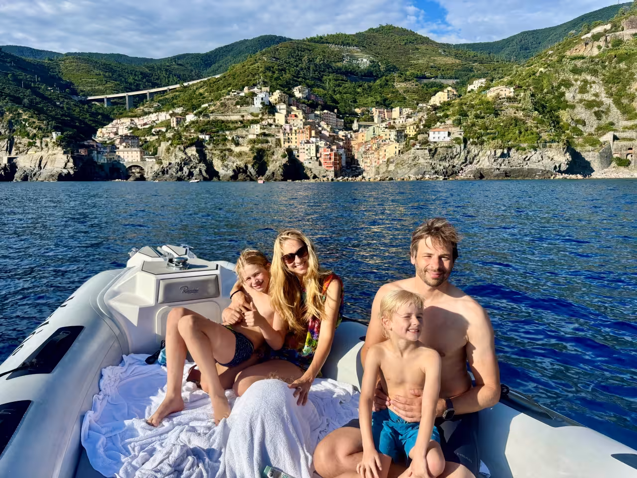 Family relaxing on a boat with Riomaggiore village views during a Cinque Terre full-day boat tour from La Spezia