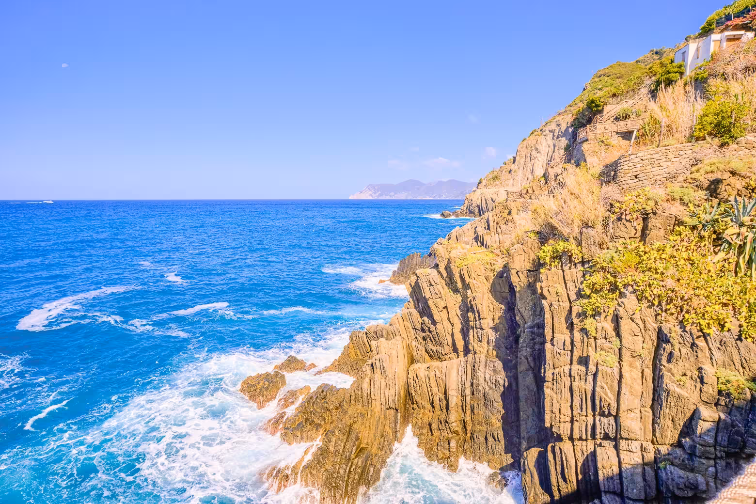 Breathtaking view of rugged cliffs and azure sea along Cinque Terre coast under clear blue skies.