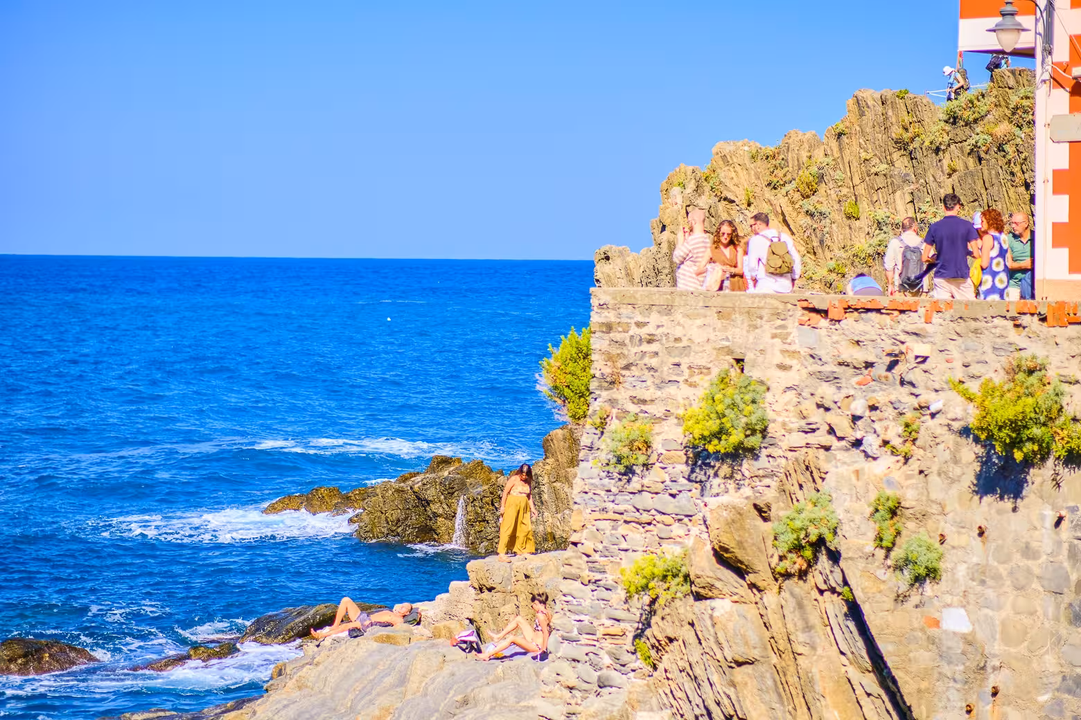 Tourists enjoying the stunning coastal view on the rocky cliffs of Cinque Terre National Park.