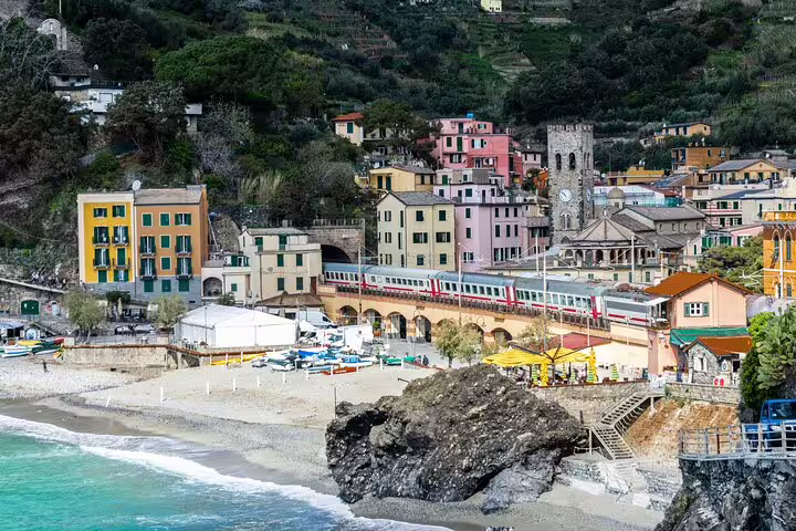 Coastal train passing pastel buildings and sandy beach in Monterosso al Mare, Cinque Terre, on a tour from La Spezia