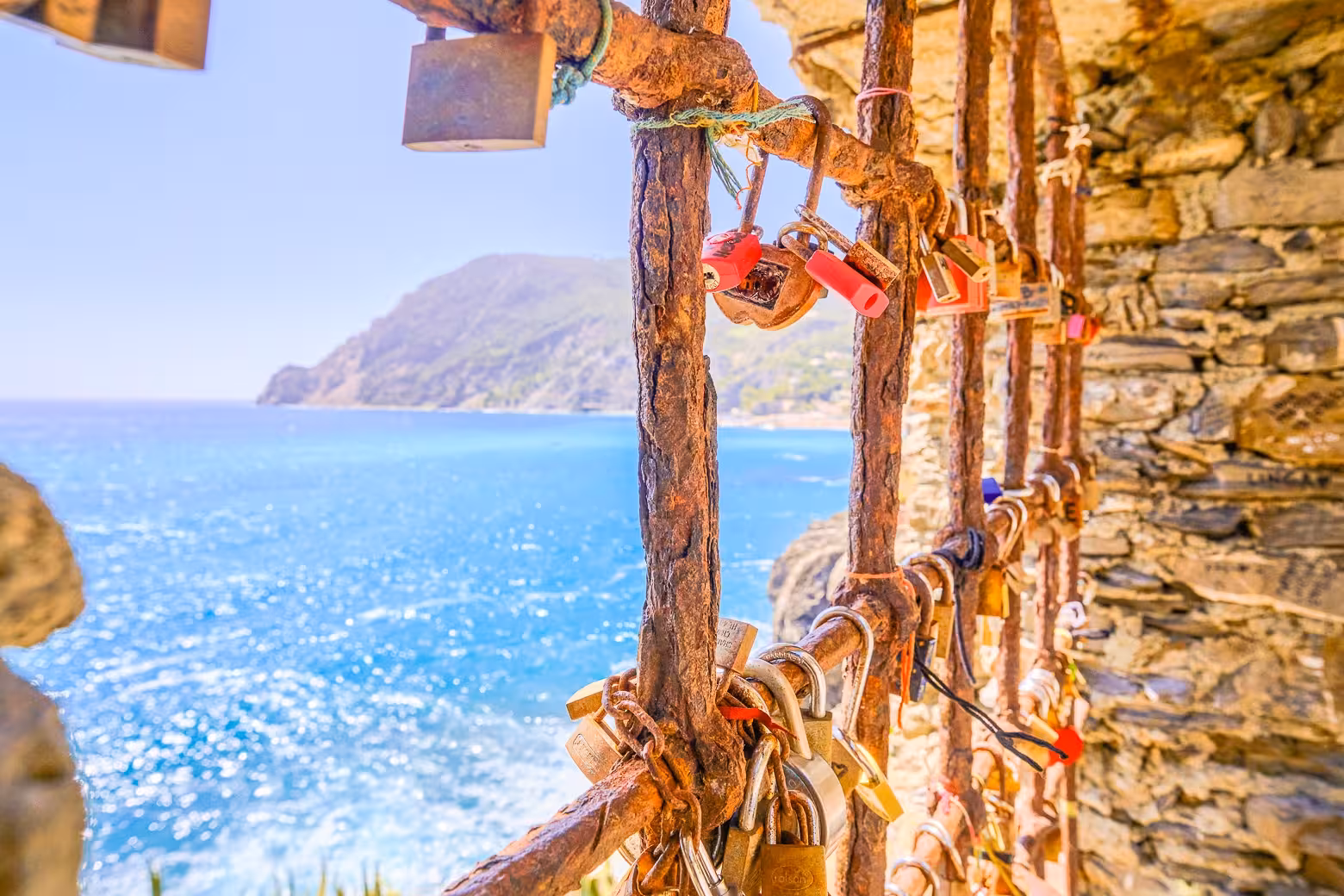 Rustic love locks hang on a fence with stunning views of the Cinque Terre coastline and azure sea.