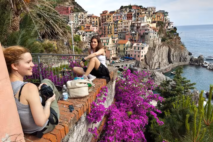 Two women relaxing with vibrant flowers overlooking Manarola, Cinque Terre, on a day trip from Florence.