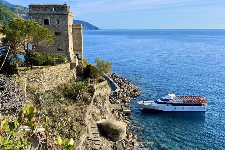 A scenic view of a historic stone tower and a boat in the clear blue waters of Monterosso al Mare, Cinque Terre.