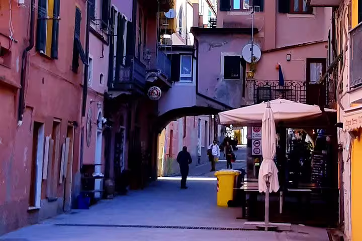Narrow pastel alley in Cinque Terre village with archway, cafés and pedestrians on a private walking tour from Porto Venere