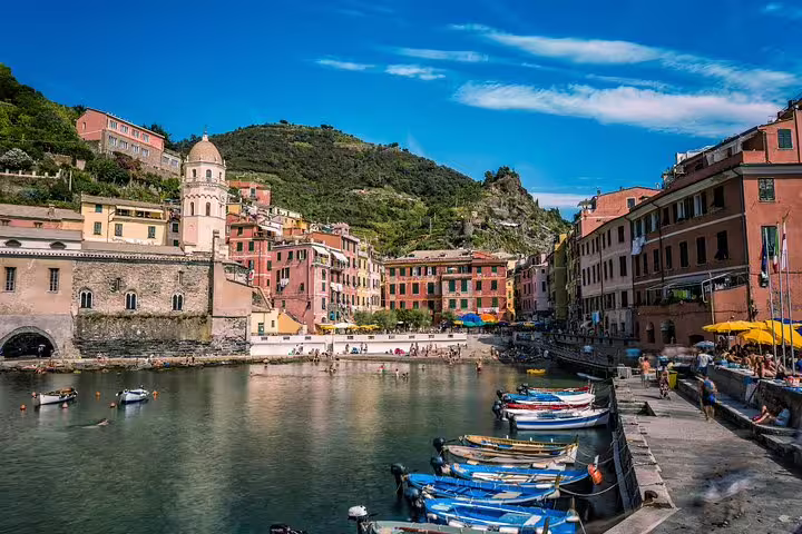 Boats bob in Vernazza harbor beneath colorful cliffside houses on a Cinque Terre and Porto Venere private day tour
