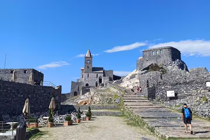 Visitor walking up ancient stone steps toward Portovenere church and fortress on a sunny La Spezia to Cinque Terre shore excursion
