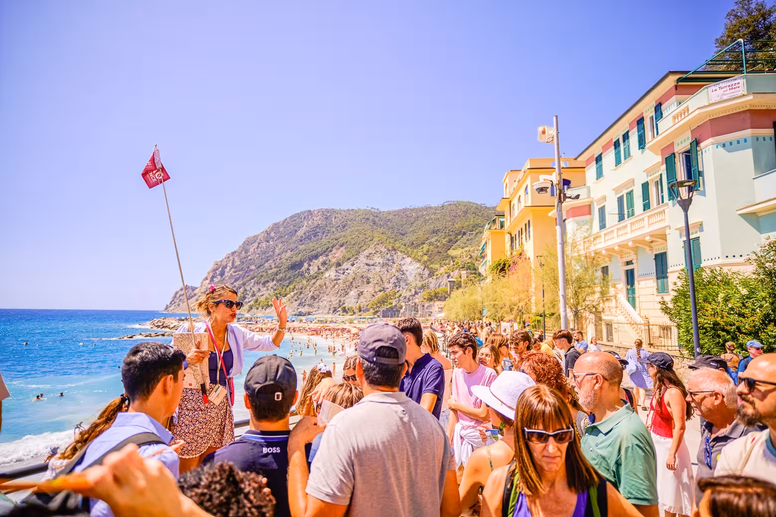 Guide leading a group through Cinque Terre's scenic coastal town with colorful buildings and beach views.