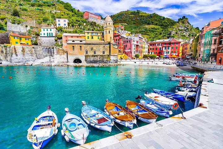 Colorful fishing boats moored in Vernazza harbor with pastel houses and church on a Cinque Terre day trip from La Spezia