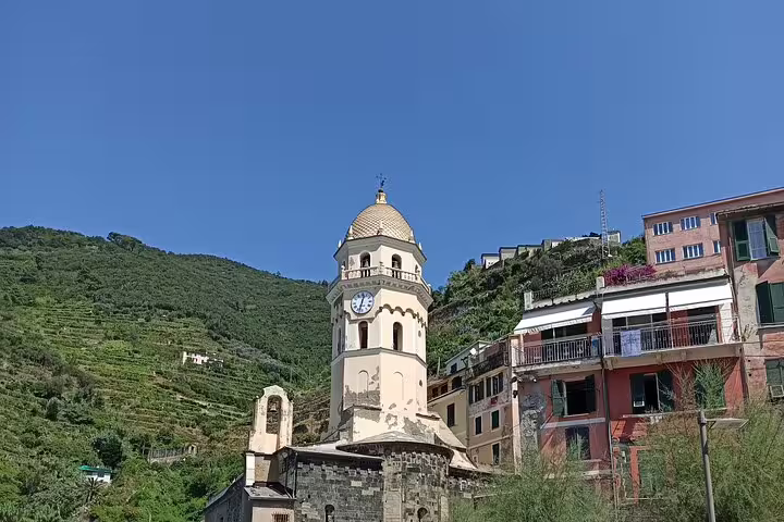 Historic church tower and colorful hillside homes in a Cinque Terre village, viewed on a clear day of a private Italy tour