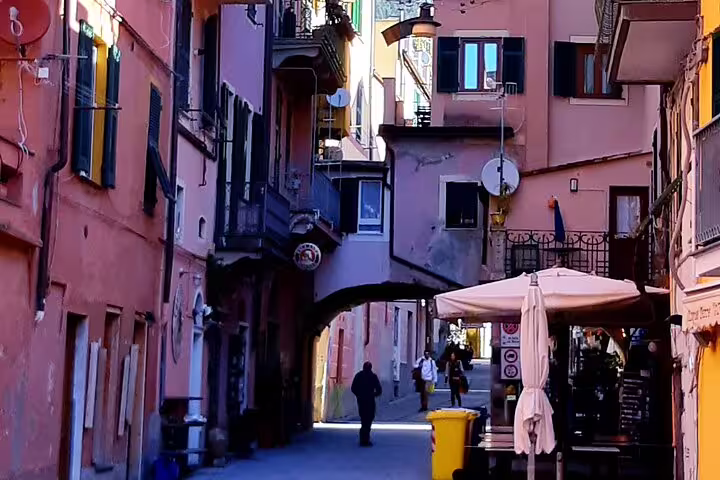 Narrow cobbled alley with pastel houses, cafes and locals in a historic Cinque Terre village reached from La Spezia port