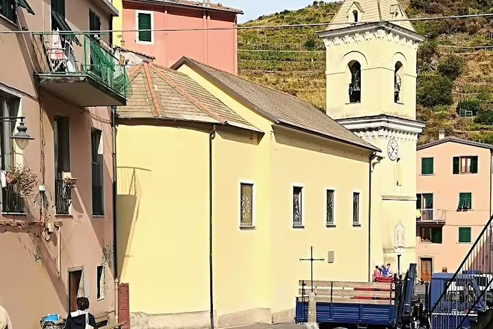 Sunlit village square in Cinque Terre with pastel church, bell tower and locals on a La Spezia shore excursion transfer