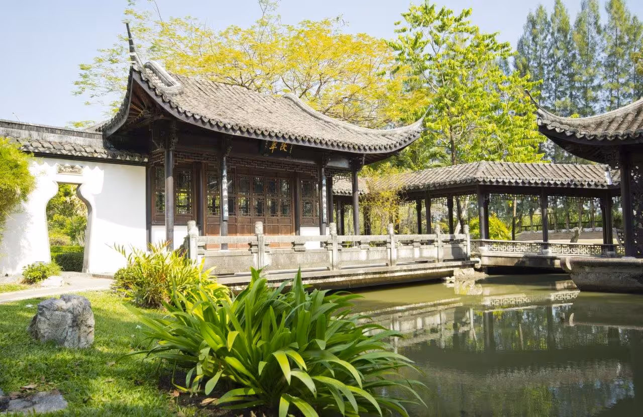 Traditional Chinese garden with wooden pavilion and serene pond, showcasing classic architecture in lush surroundings.