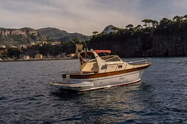 Classic Gozzo 850 boat anchored off the scenic coast of Sorrento, with lush hills and charming villas in the background.