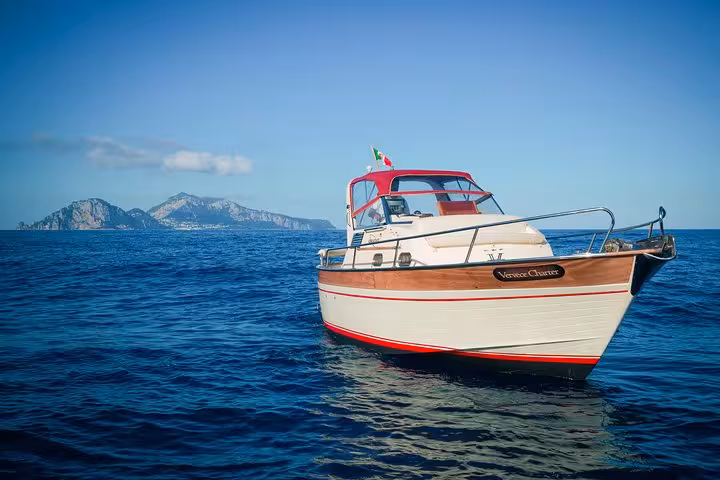 Classic Gozzo boat cruising the serene blue waters of Sorrento with Capri's scenic coastline in the background.