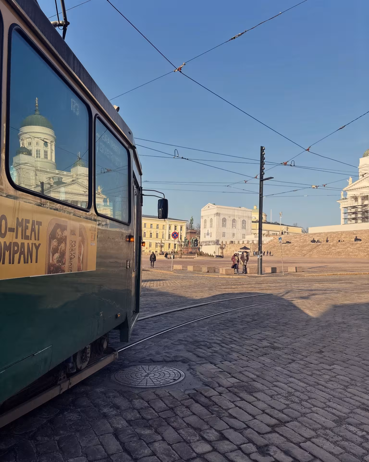 Classic tram on cobblestone street with Helsinki Cathedral in the background under clear blue skies.
