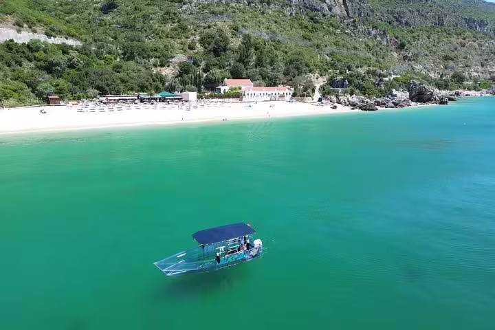A clear boat floats on the tranquil turquoise waters near Sesimbra's scenic coast, offering a unique glass bottom view.