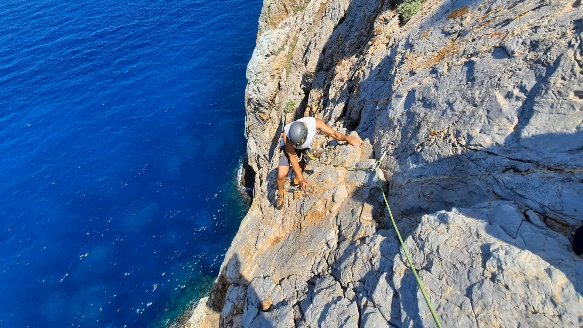 Climber navigating rocky terrain with clear blue sea backdrop at Pan di Zucchero, Italy.