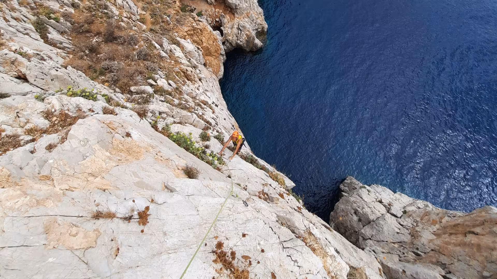 Climber scaling steep rock face above the deep blue sea at Pan di Zucchero, Sardinia.