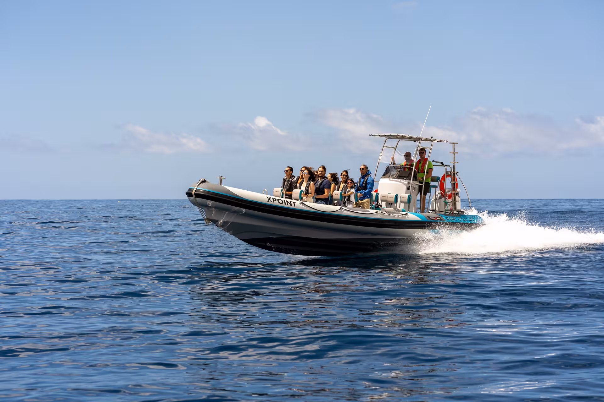 Tourists enjoy a thrilling coastal sightseeing tour on a RIB boat under a clear blue sky.