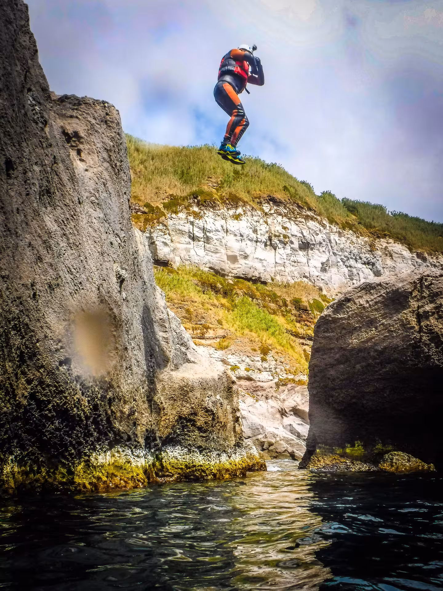 Coasteering Freshman cliff jump into the sea between rocky cliffs, wetsuit and helmet adventure tour