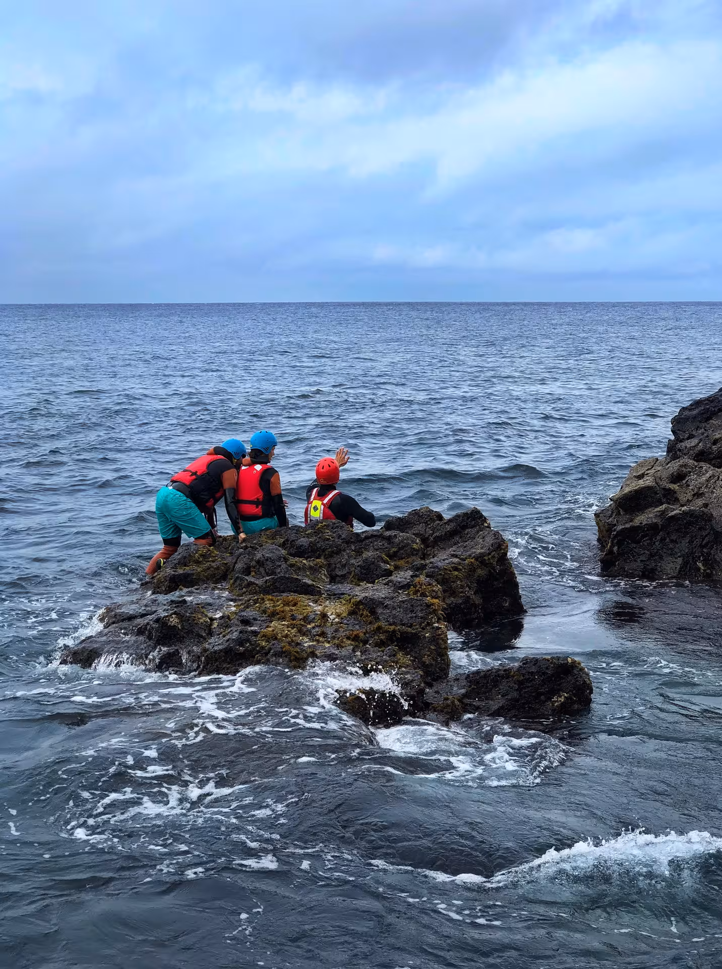 Coasteering Freshman group in helmets and buoyancy aids on sea rocks, preparing for ocean entry