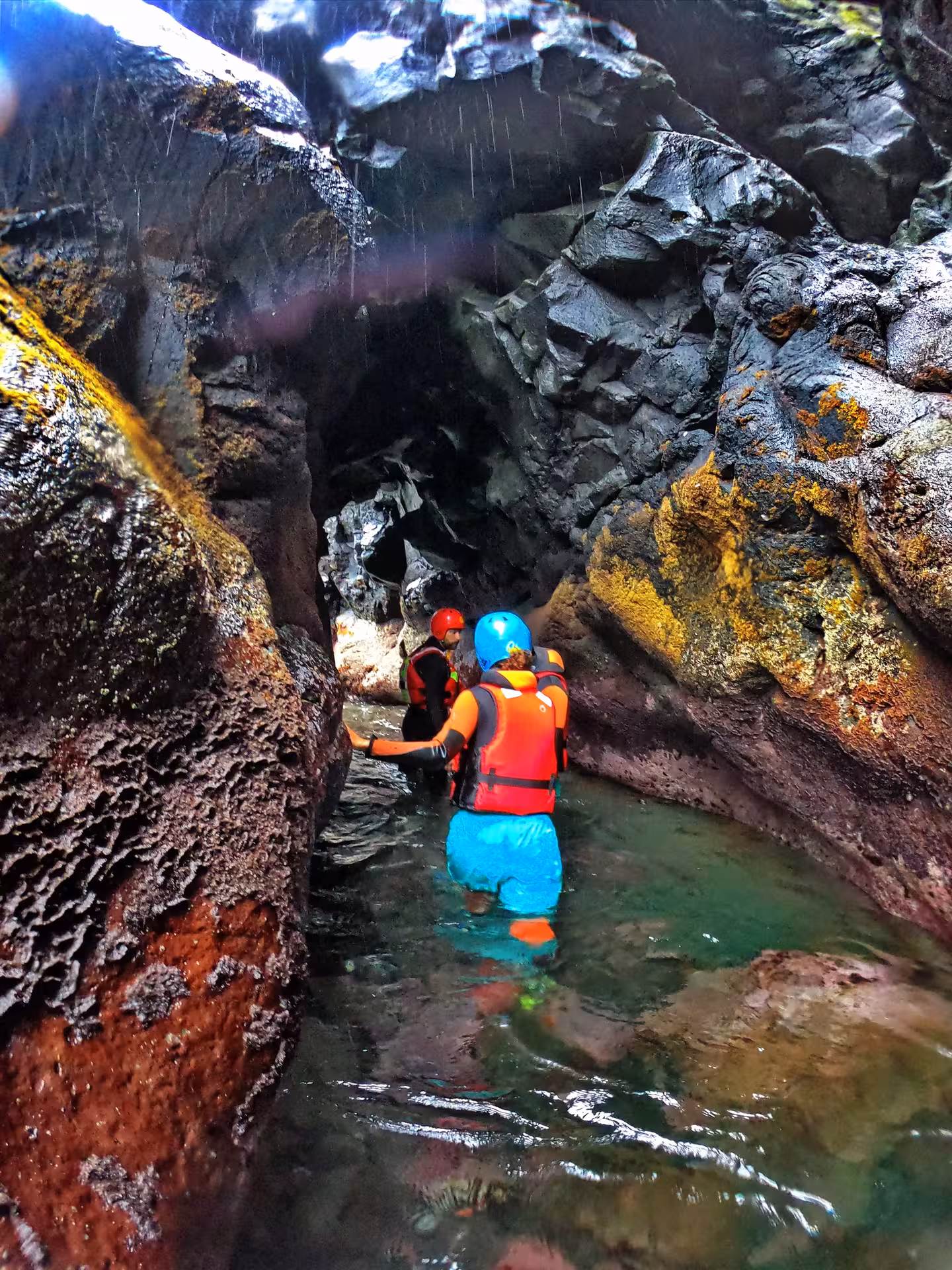 Coasteering Freshman group wading through a narrow sea gorge, helmets and buoyancy aids on guided tour