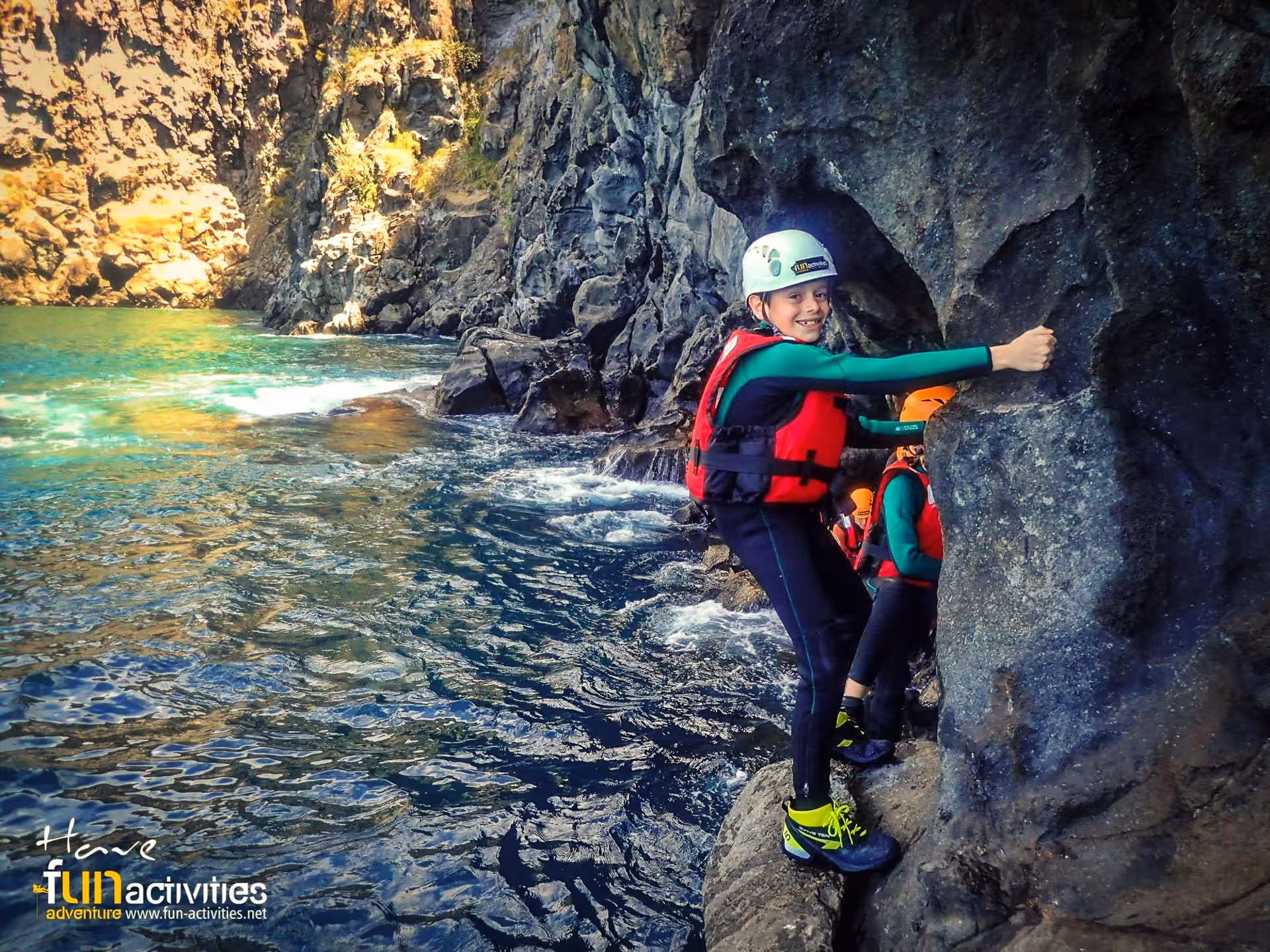COASTEERING Freshman participant traversing a rocky shoreline in wetsuit and helmet above clear water in a sea cave