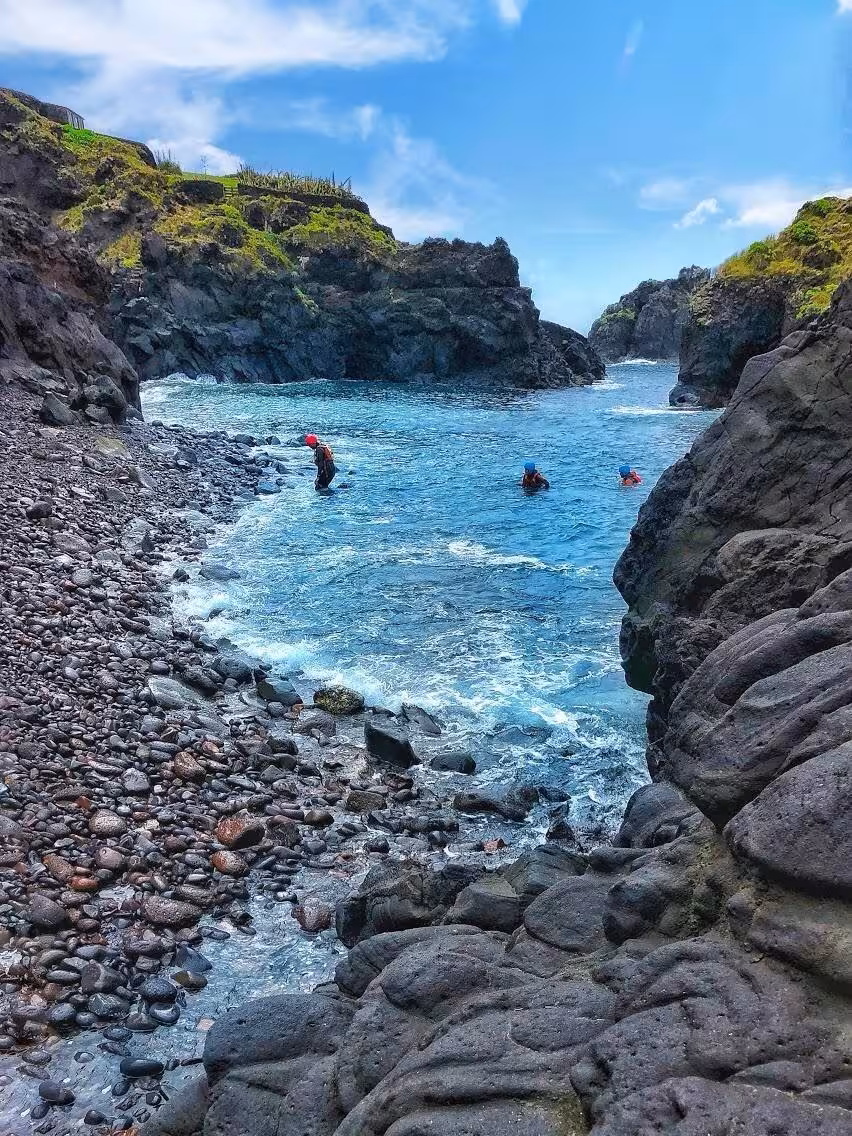 Coasteering Freshman tour swimmers in a rocky coastal cove with clear blue water, sea cliffs and pebble beach