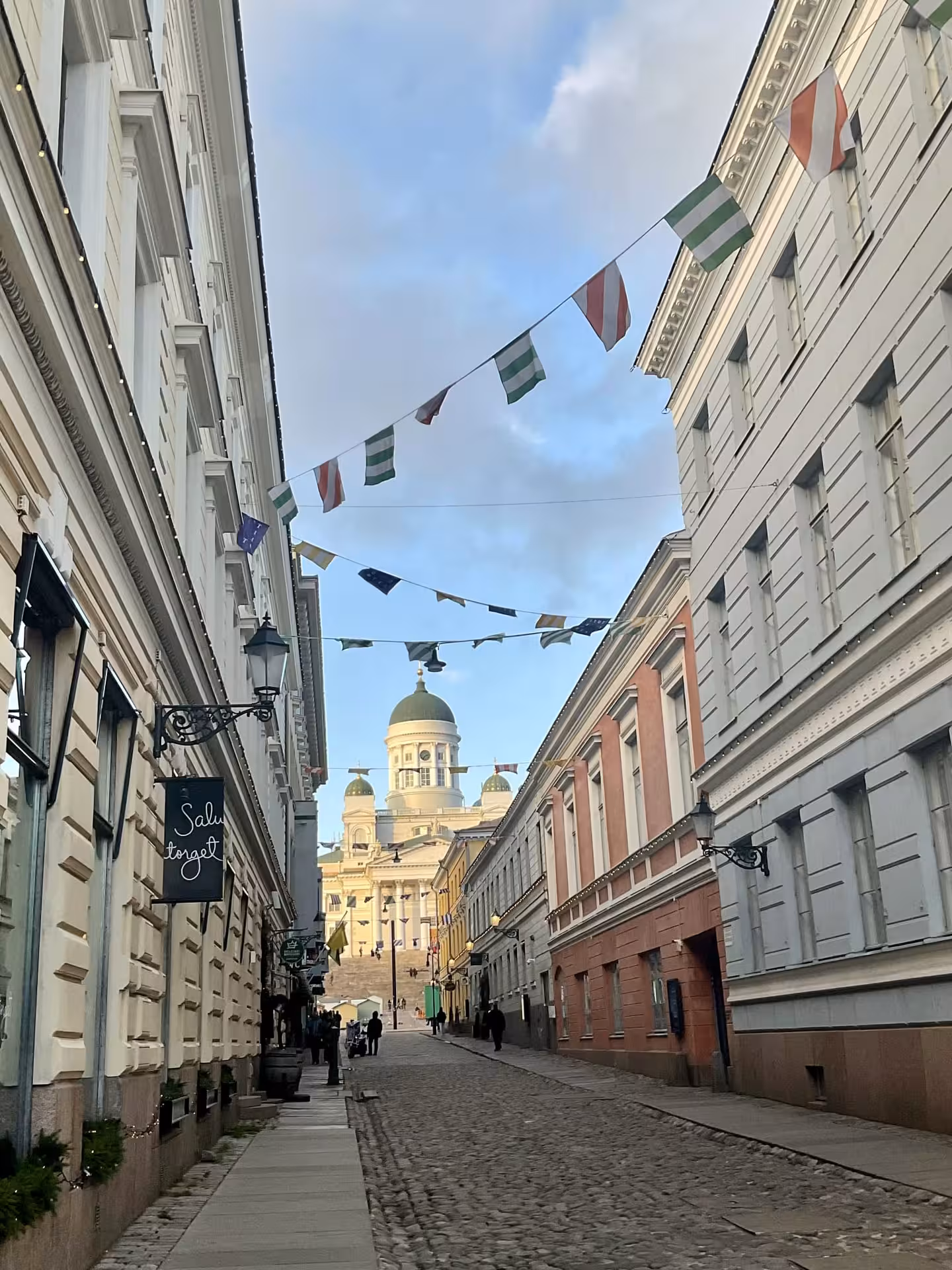 Cobblestone street leading to a grand cathedral with colorful flags, perfect for exploring architectural landmarks.