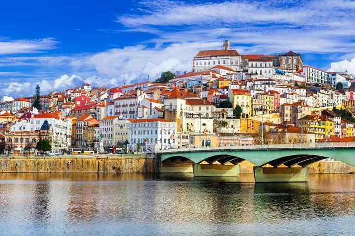 Picturesque view of Coimbra's colorful hillside buildings with a serene river foreground, seen on the Porto tour.