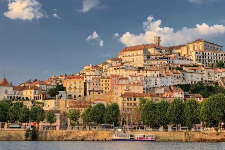 Scenic view of Coimbra's historic hillside architecture along the Mondego River, featured in a full-day tour from Lisbon to Tomar and Coimbra.