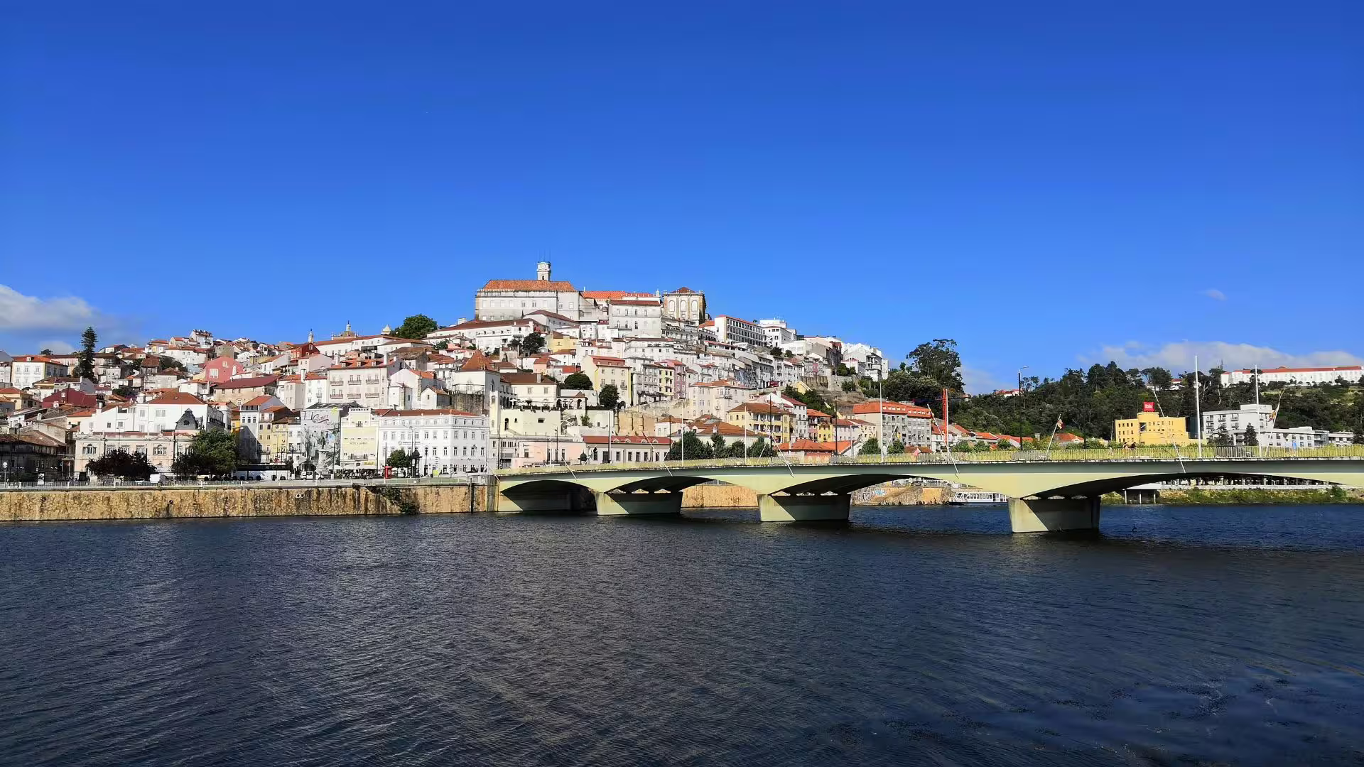 Scenic view of Coimbra's historic architecture overlooking the Mondego River on a sunny day.