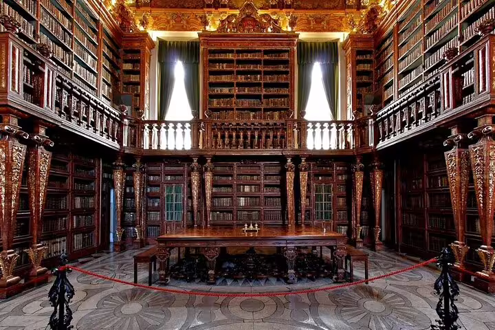 Ornate library interior in Coimbra, showcasing intricate wooden bookshelves and historic architecture on a Lisbon to Tomar tour.