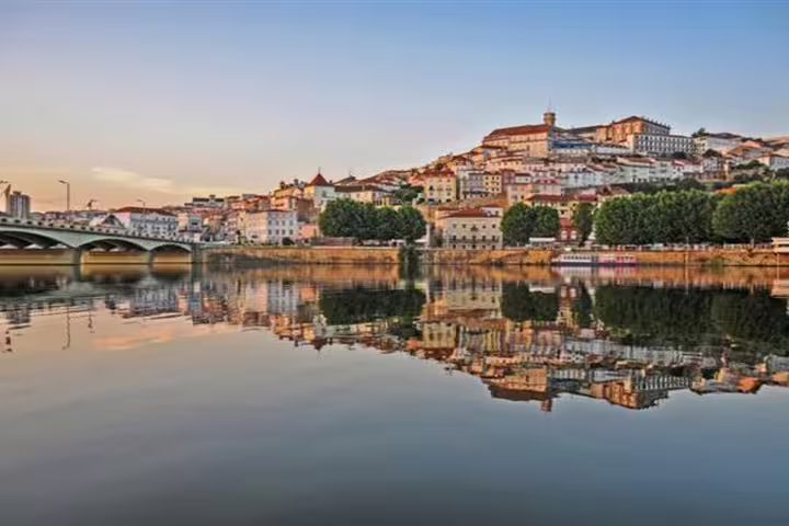 Scenic view of Coimbra's historic hillside architecture reflected in the Mondego River during a private transfer from Lisbon to Porto.